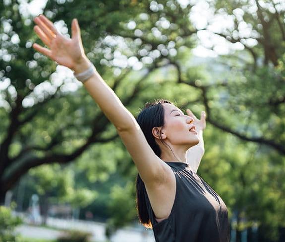 Young Asian sports woman with eyes closed stretching with arms outstretched.